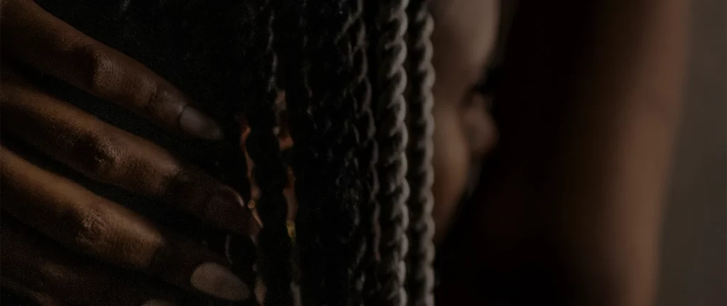 Tmavé pozadí s detailem zapletených vlasů pro stránku kurzů pletení